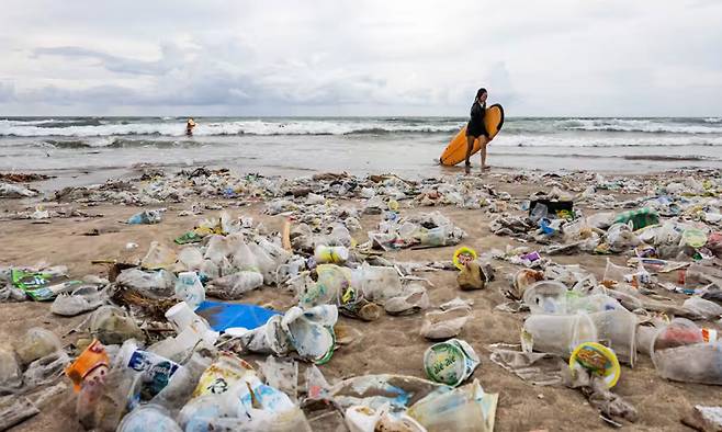 2024년말 쓰레기가 쌓여있는 인도네시아 발리의 해변을 여행객이 서핑보드를 들고 지나가고 있다. 발리=EPA연합뉴스