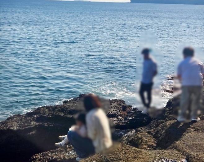 용머리해안 일대에서 외국인 관광객 일행이 바다를 배경으로 모여 있는 모습. 왼쪽 아래에는 논란이 된 여성 관광객과 아이가 포착됐다. (온라인 커뮤니티 캡처)