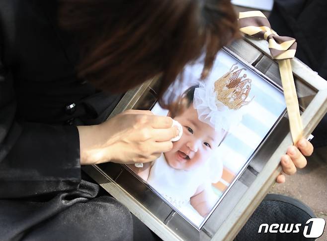 16개월 된 입양아 정인양을 학대해 숨지게 한 혐의를 받는 양부모의 1심 선고공판이 열린 지난 2021년 5월 14일 오후 양천구 서울남부지방법원 앞에서 상복을 입은 한 시민이 정인이 사진을 닦고 있다. 2021.5.14/뉴스1 ⓒ News1 구윤성 기자