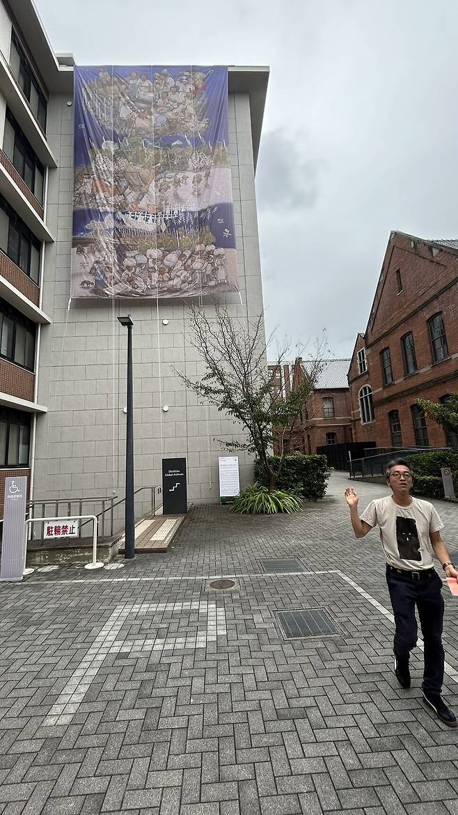 지난 12일 일본 교토 도시샤대학 후소칸 건물 외벽에는 우토로마을 주민들의 삶을 기록한 대형 걸개그림 ‘피어라, 민들레’가 걸려 있다. 유재현 페스티벌 예술감독이 걸개그림의 의미를 설명하고 있다.