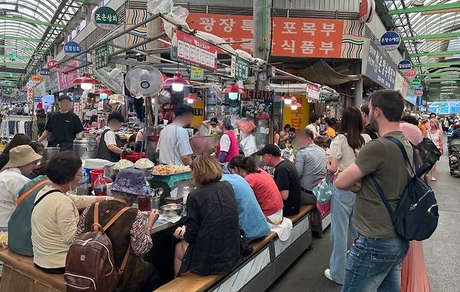 서울 광장시장의 한 가판에서 외국인 관광객들이 한국 음식을 맛보고 있다. /뉴스1