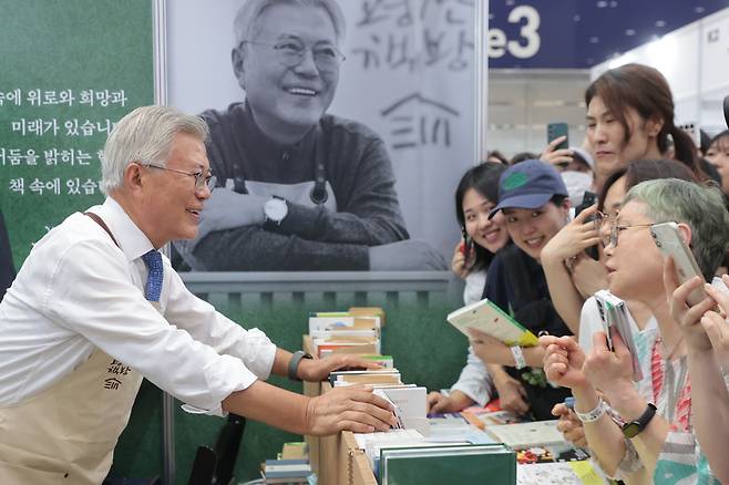 Former President Moon Jae-in (left) greets visitors at his booth at the 2025 Seoul International Book Fair on Wednesday at Coex. (Yonhap)
