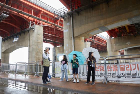 김효(왼쪽) 한강역사해설사에게 과거 최고 홍수위라는 기준표와 을축년 대홍수에 대한 설명을 듣고 있는 소중 학생기자단.