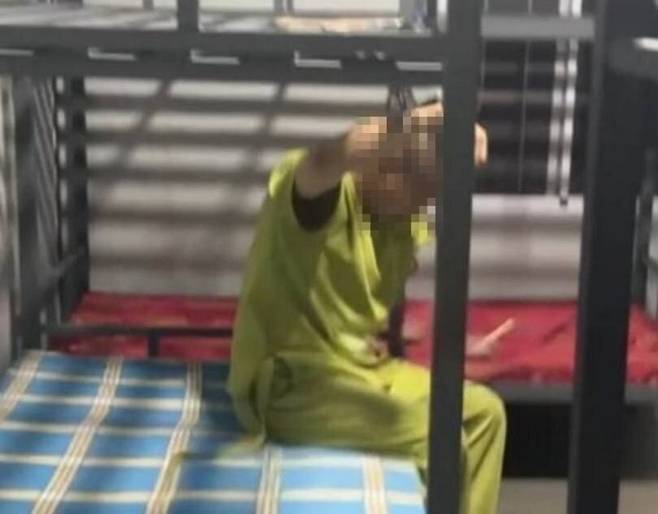 캄보디아 내 한 웬치(범죄단지)의 납치·감금자가 팔에 수갑이 채워진 채 침대에 앉아 있다. 연합뉴스