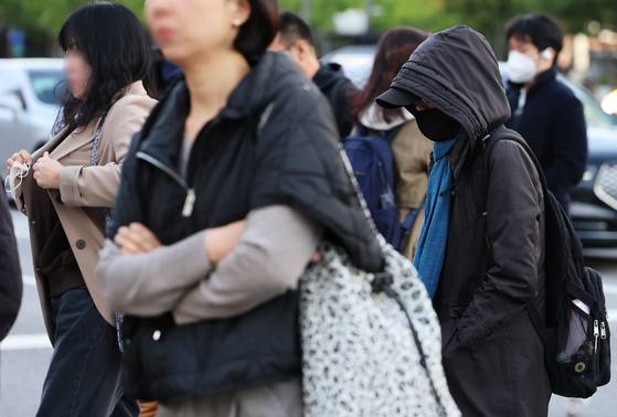 Commuters bundle up against the unseasonably early winter chill, with morning temperatures dropping to 4.8 degrees Celsius in Seoul, as they hurry through an intersection near Gwanghwamun on Oct. 21. [NEWS1]