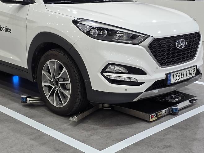 ▲ HL로보틱스가 22일 FIX 2025 개막 현장에서 자율주행 주차로봇의 주차 과정을 시연하고 있다. 차량 하부로 들어간 로봇이 양날개를 펼쳐 차량 앞타이어를 들어올리고 있다. 전재용 기자