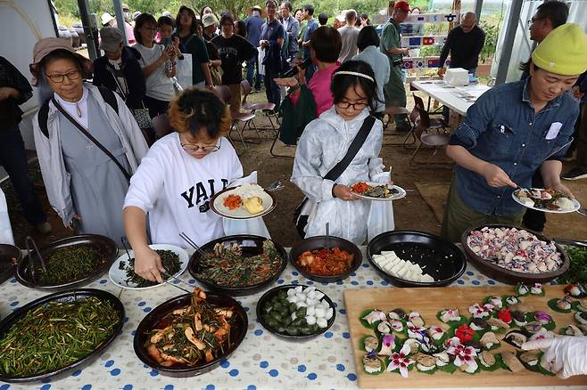 평화마을짓자 가을잔치 참가자들이 공동체 밭에서 거둔 식재료 등으로 차린 ‘기후밥상\' 음식을 접시에 담고 있다.