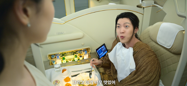 드라마 '다 이루어질지니'에서 지니 역을 맡은 김우빈(오른쪽)이 비행기 기내식을 먹으며 "이거 너무 맛있어"라고 말하고 있다. 이 기내식 서비스를 제공하는 아랍에미리트 항공사인 에미레이트가 간접광고(PPL) 투자사로 참여했다. 넷플릭스 오리지널 드라마에서 대사를 통해 노골적인 PPL이 노출되기는 이례적이다. 넷플릭스 영상 캡처