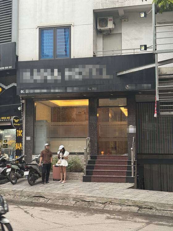 A man smokes in front of a hotel in Hanoi after dropping off a young woman on a motorcycle. Transporting women by motorcycle to hotels and karaoke bars catering to Korean men is a common scene. [WOMEN MIGRANTS HUMAN RIGHTS CENTER OF KOREA]