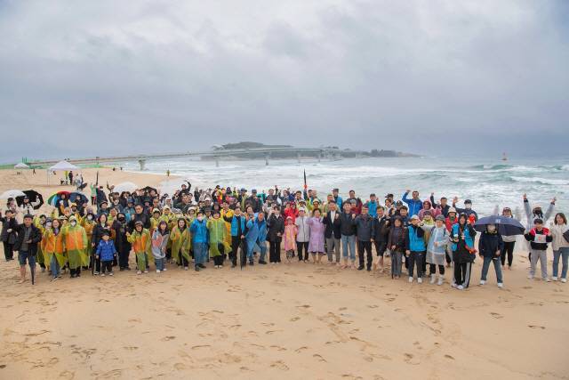 ▲ 8일 ‘2025 글로벌 평화경제특구 지정 기원 고성군 송지호 대섬 맨발걷기 페스타’ 참가자들이 한 곳에 모여 송지호 대섬과 해양스카이워크가 조망되는 포토 존에서 단체 기념 촬영을 하고 있다.