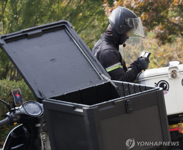 지난달 31일 오후 서울 서초구의 한 건물 앞에서 한 배달 노동자가 음식 배달을 마친 뒤 스마트폰을 바라보고 있다. ⓒ연합뉴스