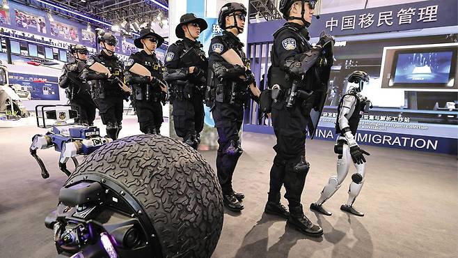 올해 베이징에서 열린 ‘국제 경찰 장비 박람회’에서 경찰들이 휴머노이드 로봇과 순찰 훈련을 하고 있다. 두꺼운 타이어처럼 생긴 이 로봇은 지명수배자를 식별할 수 있다./신화 연합뉴스