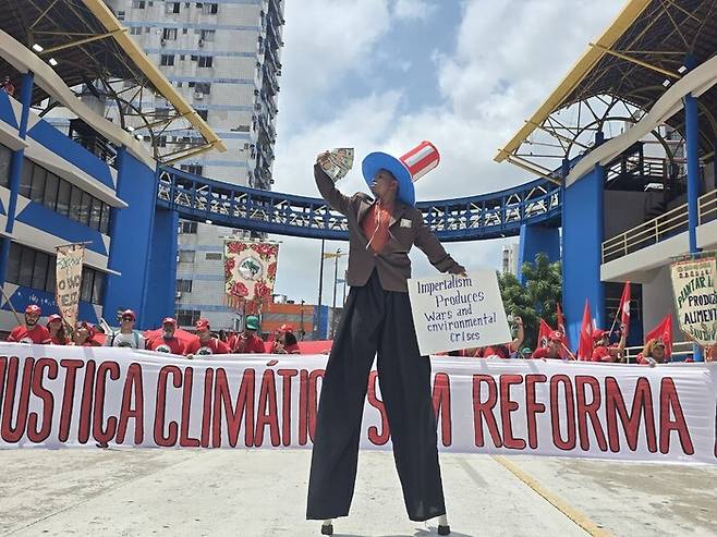 15일 브라질 벨렝에서 열린 민중정상회의 행진에서 한 참가자가 미국 도널드 트럼프 대통령의 얼굴이 그려진 돈을 들고 행진 도중 퍼포먼스를 하고 있다. 벨렝/옥기원 기자 ok@hani.co.kr