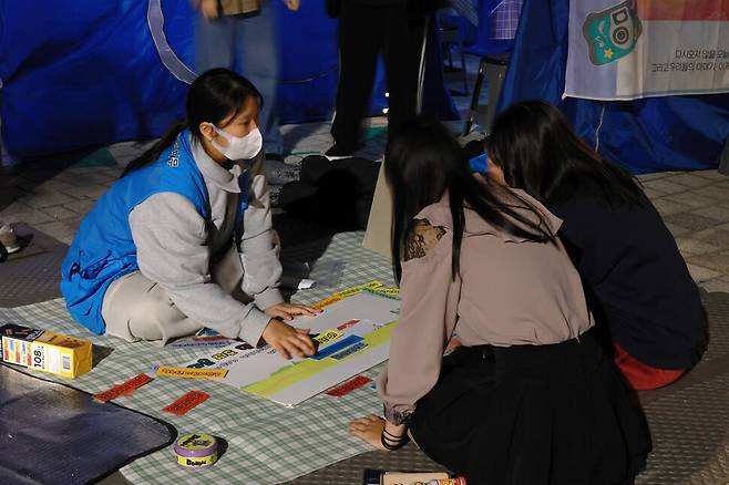 8일 저녁 서울 마포구 홍대입구역 6번 출구 인근에 설치된 ‘서울시립십대여성일시지원센터 나무’ 상담 천막 앞에서 한 활동가가 청소년들과 함께 마을 지도를 만들며 받을 수 있는 지원 정책을 설명하고 있다. 김혜윤 기자 unique@hani.co.kr
