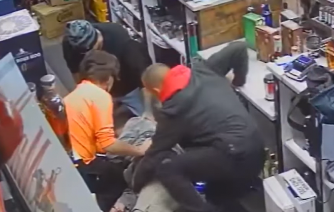 빨간색 후드티를 입은 한 남성이 심장마비로 쓰러진 주류 판매점 직원을 돕는 척 그의 몸을 더듬고 있다. 유튜브 채널 ‘KPTV 폭스12’ 캡처