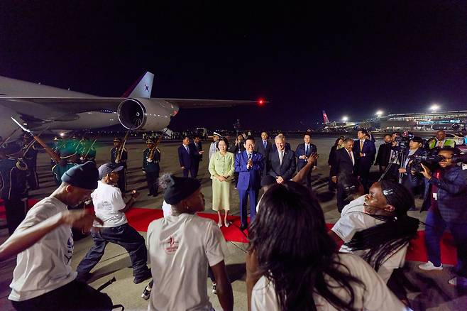 이재명 대통령과 김혜경 여사가 21일(현지 시각) 밤 남아프리카공화국의 요하네스버그에 도착해, 공항에서 환영 공연을 보며 박수를 치고 있다./연합뉴스
