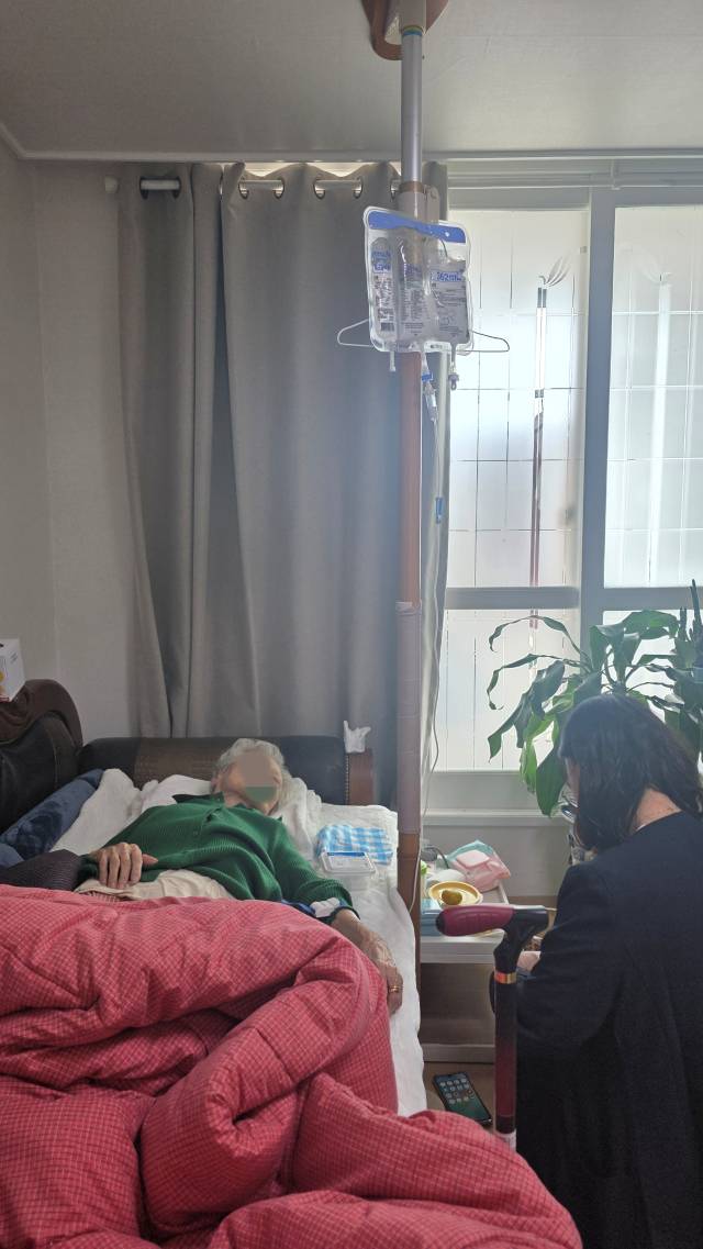 기승국 홈닥터예방의학과의원 원장과 함께 거동이 불편해져 병원 방문이 어려운 어르신의 집을 방문한 강소윤(오른쪽) 간호사가 수액 투여를 준비 중이다. 입원 병실처럼 폴대가 없으니 침대 옆에 설치된 낙상 방지봉에 옷걸이를 부착해 영양수액제를 걸었다. 안경진 기자