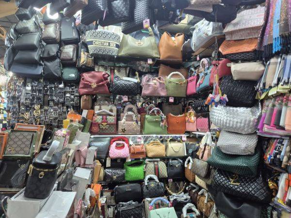 좁은 상점 벽면을 따라 수백 개의 명품 로고 가방이 층층이 걸려 있어, 벽 자체가 가방으로 덮여 있는 듯했다.