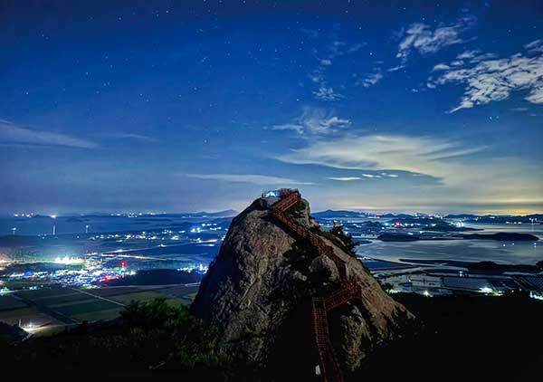 무수히 많은 섬을 품은 신안의 바다와 쏟아질 것 같은 별을 품은 밤하늘을 배경으로 담은 투구봉의 야경. 전망대의 텐트가 북극성처럼 빛나고 있다.