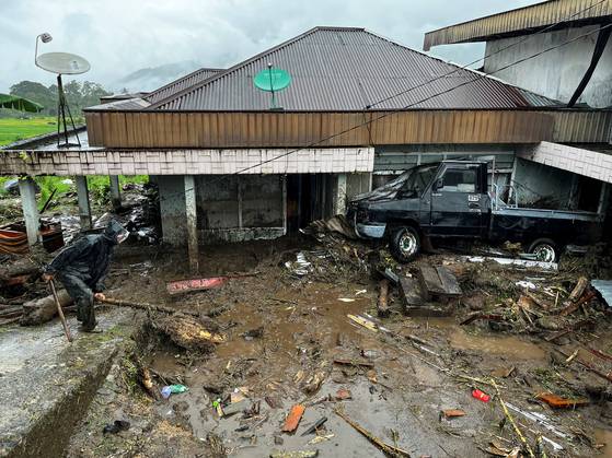 28일(현지시간) 인도네시아 서수마트라 주 아감의 말락에서 폭우로 인한 홍수로 집 옆에 차량이 갇혀 있는 가운데 한 주민이 나뭇가지를 제거하고 있다. 로이터=연합뉴스