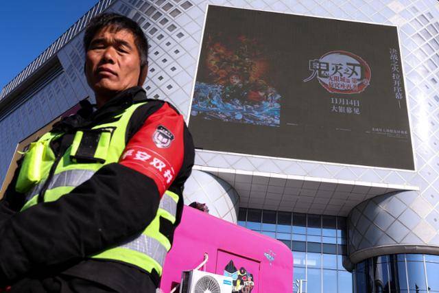 중국 경비원이 지난 18일 베이징 시내 쇼핑몰 외벽 대형 스크린 앞에 서 있다. 스크린에는 일본 애니메이션 '귀멸의 칼날' 홍보 영상이 나오고 있다. 베이징=로이터 연합뉴스