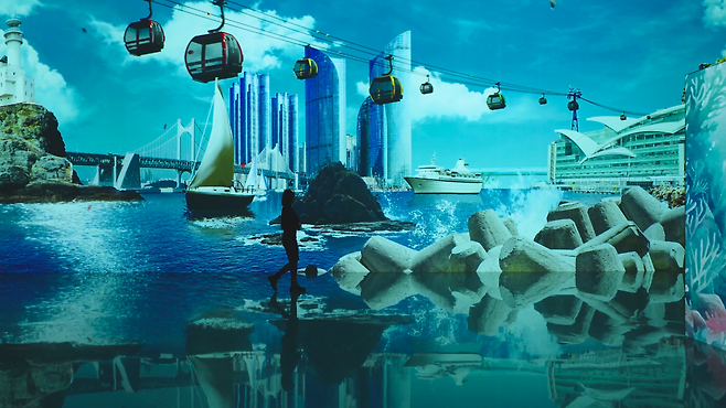 부산의 명소를 나타낸 미디어아트 전시물 앞을 걸어가는 관람객 (영상 출처: 부산관광공사)