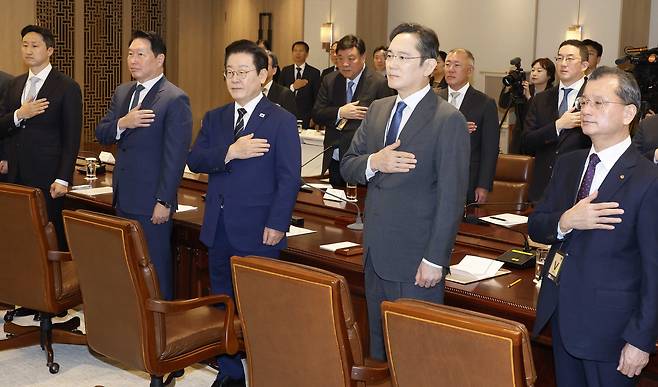 President Lee Jae Myung, center, and the heads of top Korean conglomerates, including SK Group Chairman Chey Tae-won, seccond from left, and Samsung Electronics Executive Chairman Lee Jae-yong, second from right, salute the flag before a joint government and private sector meeting at the presidential office in Yongsan, central Seoul on Nov. 16. [JOINT PRESS CORPS]