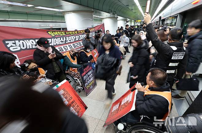 [서울=뉴시스] 이영환 기자 = 전국장애인차별철폐연대(전장연) 회원들이 4일 오전 서울 종로구 지하철5호선 광화문역에서 열린 '제67차 출근길 지하철 탑니다’ 시위를 하는 가운데 시민들이 이동하고 있다. 2025.12.04. 20hwan@newsis.com