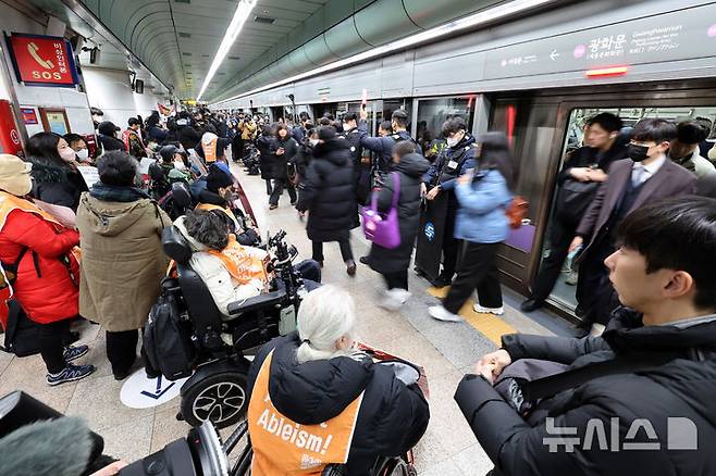 [서울=뉴시스] 이영환 기자 = 전국장애인차별철폐연대(전장연) 회원들이 4일 오전 서울 종로구 지하철5호선 광화문역에서 열린 '제67차 출근길 지하철 탑니다’ 시위를 하는 가운데 시민들이 이동하고 있다. 2025.12.04. 20hwan@newsis.com