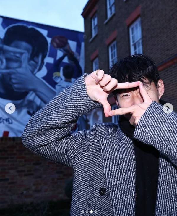 Former Tottenham Hotspur player Son Heung-min poses with his signature camera clicking hand gesture in front of a mural outside of the Totthenham Hotspur Stadium in London in this screen capture from Tottenham Hotspur's Instagram. [SCREEN CAPTURE]