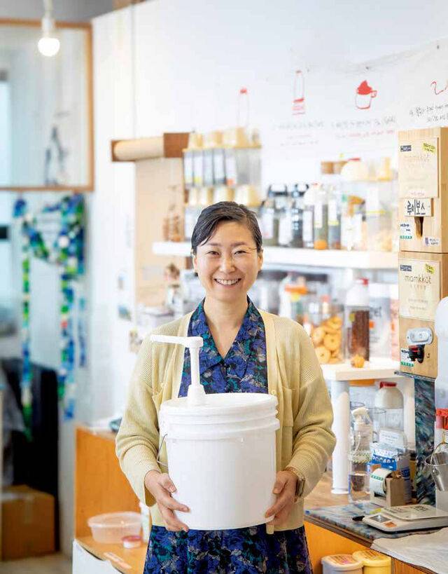 고금숙 공동대표가 ‘알맹상점’에서 리필 제품이 든 말통을 들고 환히 웃고 있다.