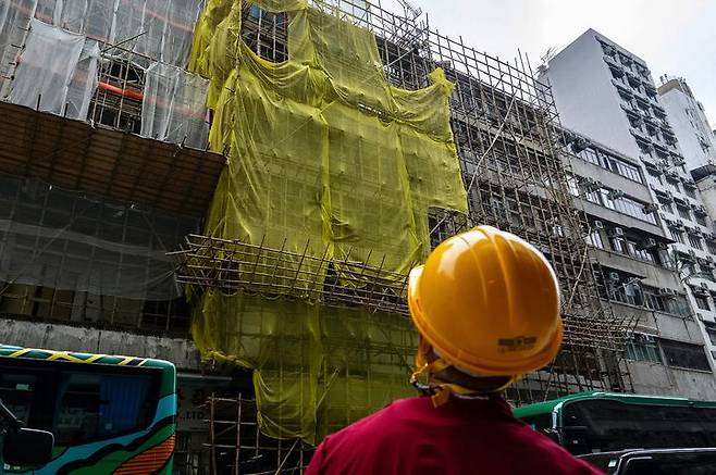 [홍콩=AP/뉴시스] 홍콩에서 군대식 훈련을 하던 시민들이 잇따라 ‘정부 전복혐의’ 등으로 체포되고 일부는 기소됐다고 홍콩 사우스차이나모닝포스트(SCMP)가 14일 보도했다. 사진은 지난 4일 홍콩 몽콕 지역의 한 건물 보수 공사 현장에서 노동자들이 그물망을 제거하는 모습. 2025.12.15.
