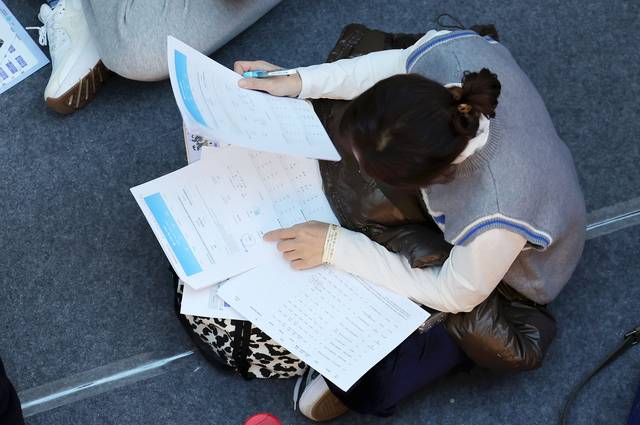 정시 전략 어쩌나  : 18일 오전 서울 강남구 코엑스에서 열린 2026학년도 정시 대학입학정보박람회를 찾은 한 학부모가 행사장 입장 전 바닥에 앉아 입시 자료를 살펴보고 있다.  뉴시스