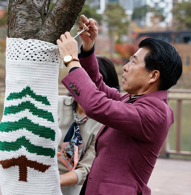 Songpa-gu Mayor Seo Kang-seok attaches a knitted cover to a tree. (Courtesy of Songpa District Office)