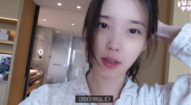 아이유는 해외 일정으로 도착한 호텔에서 막 잠에서 깬 모습으로 카메라 앞에 섰다. 사잔-유튜브 채널 ‘이지금’