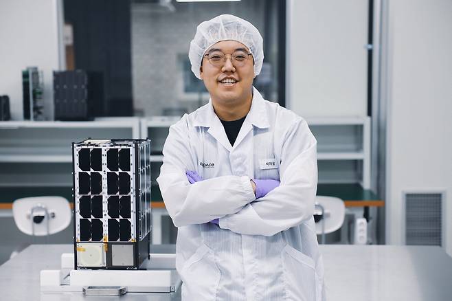 박재필 나라스페이스테크놀로지 대표가 초소형 위성 모형 옆에서 웃고 있다.