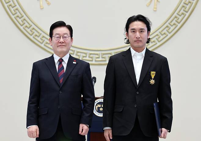 President Lee Jae Myung, left, poses with director Shin Woo-seok of the production crew Dolphiners Films after presenting him with the Mongnyeon Medal, a fourth-highest rank of the Order of Civil Merit, during the 2026 New Year’s gathering at the state guesthouse of the Blue House in central Seoul on Jan. 2. [NEWS1]