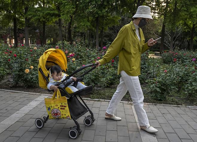 2021년 5월, 중국 베이징의 한 공원에서 한 여성이 유모차를 끌고 휴대폰을 바라보고 있다. 게티이미지