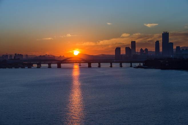 The sun rises over the Han River in December 2013. High-rise buildings in the financial district of Yeouido, western Seoul, are visible to the right, beyond Yanghwa Bridge. [PARK JONG-GEUN]