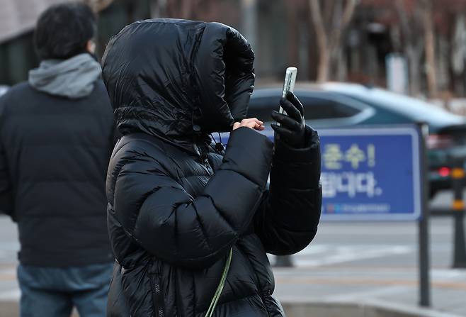 A commuter bundled up against the cold takes a photo with her phone at Gwanghwamun Intersection in central Seoul on Jan. 8, as severe cold weather returns. (Yonhap)