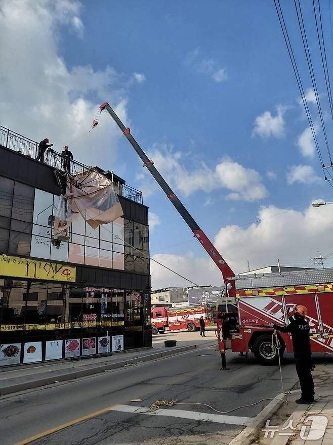 경기 고양시 일산 옥상에 설치되어 있는 캐노피 천막 구조물이 강풍으로 탈락돼 소방당국이 크레인을 활용해 지상으로 인양 작업을 벌이고 있다. (경기소방재난본부 제공. 재판매 및 DB금지)