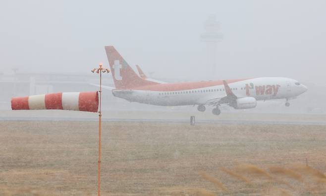 An aircraft lands on the runway at Jeju International Airport while snow falls on Jan. 11, as strong wind and wind shear alerts remain in effect. [YONHAP]