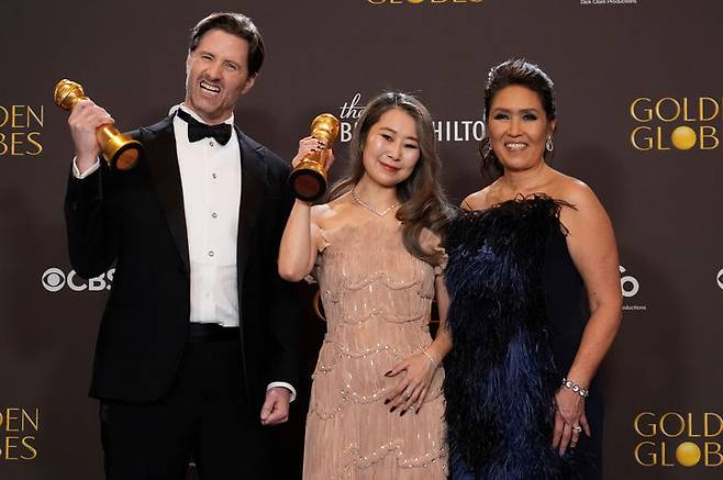 [비벌리힐스=AP/뉴시스] 매기 강(가운데) 감독이 11일(현지 시간) 미 캘리포니아 로스앤젤레스 베벌리힐스의 베벌리힐튼에서 열린 제83회 골든글로브 시상식에서 '케이팝 데몬 헌터스'(케데헌)로 애니메이션 작품상(장편 애니메이션)을 받은 후 기자실에서 크리스 애펄헌즈(왼쪽) 공동 연출자, 매기 웡 소니 프로듀서와 기념 촬영을 하고 있다. 2026.01.12.