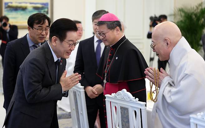 President Lee Jae Myung, left, greets Ven. Jinwoo, president of the Jogye Order of Korean Buddhism, right, during a luncheon with religious leaders at the Blue House in Seoul on Jan. 12. At the center is Archbishop Peter Chung Soon-taick of the Archdiocese of Seoul. The luncheon was attended by senior leaders from Buddhism, Catholicism, Protestant Christianity, Won Buddhism, Confucianism and Cheondoism. [YONHAP]