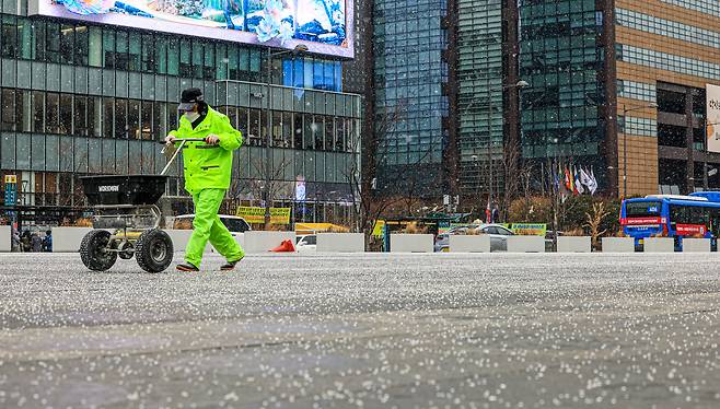 Workers spread calcium chloride at Gwanghwamun Square in central Seoul on Jan. 12 as snow falls. [NEWS1]