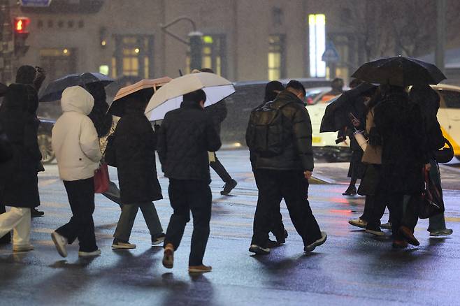People walk through Gwanghwamun Square in Jongno District, central Seoul, using hoods and umbrellas as it snows on Jan. 12. [YONHAP]