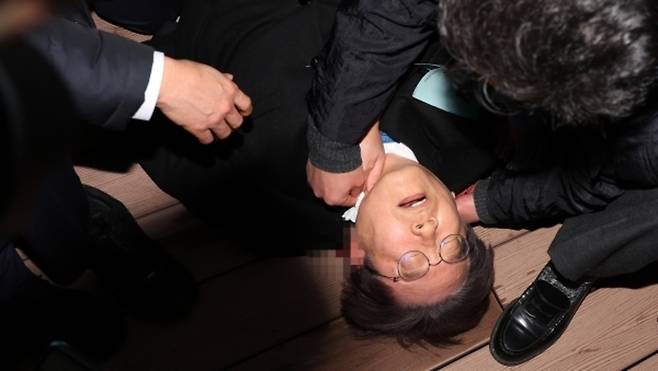 ▲ 더불어민주당 이재명 대표가 2일 부산 가덕도 신공항 부지를 둘러본 후 기자들과 문답을 진행하던 중 왼쪽 목 부위에 습격을 당해 피를 흘린 채 쓰러져 있다. /연합뉴스