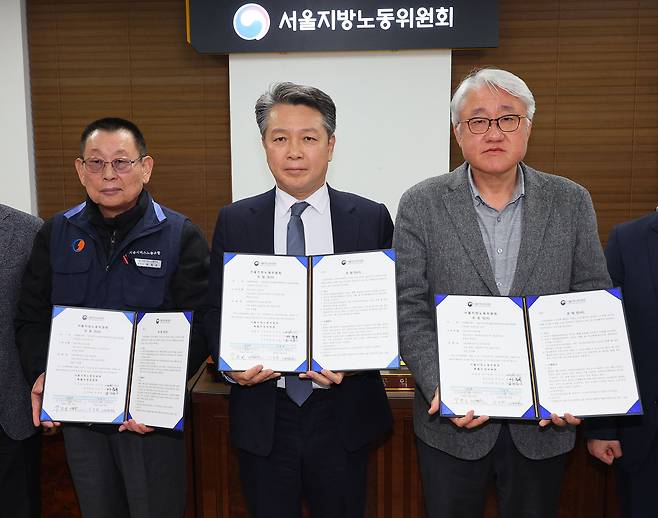 Park Jeom-gon, left, leader of the Seoul Bus Drivers Labor Union, poses for a photo with Kim Jeong-hwan, right, head of the Seoul Bus Operators Association, at the Seoul Regional Labor Relations Committee in the capital on Jan. 15, after reaching a collective wage deal with management, ending a two-day strike that caused major disruptions for commuters. [YONHAP]