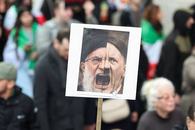 18일(현지시간) 영국 런던에서 이란 반정부 연대 시위 도중 한 시위자가 아야톨라 세예드 알리 하메네이 이란 최고지도자와 아돌프 히틀러의 얼굴을 겹친 모습의 팻말을 들고 있다. 로이터=연합뉴스