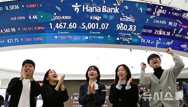 [서울=뉴시스] 최진석 기자 = 코스피가 꿈의 숫자로 여겨지던 '오천피'에 도달하며 코스피 5000 시대가 열린 22일 오전 서울 중구 하나은행 딜링룸에서 관계자들이 코스피 5000 돌파를 축하하고 있다. 코스피는 전 거래일(4909.93)보다 77.13포인트(1.57%) 상승한 4987.06에 개장했다.2026.01.22. myjs@newsis.com